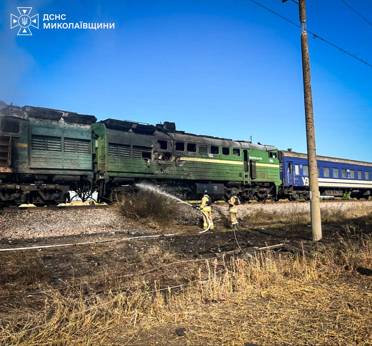 Рятувальники поливають водою обгорілий зелений локомотив біля синього вагона