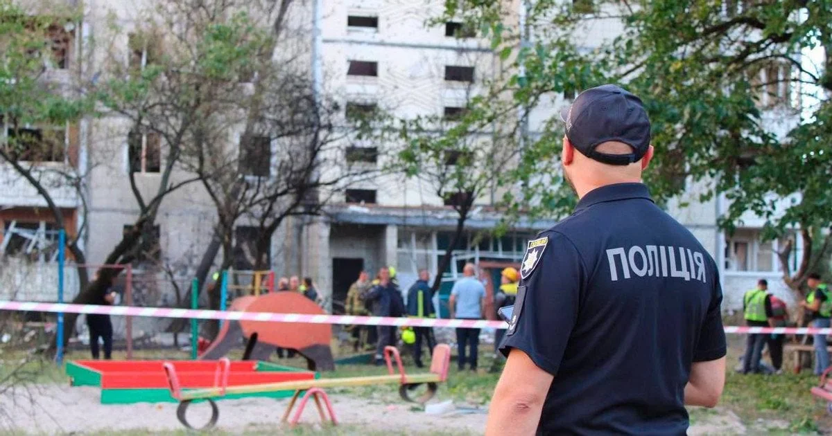 Поліцейський біля дитячого майданчика перед пошкодженою багатоповерхівкою
