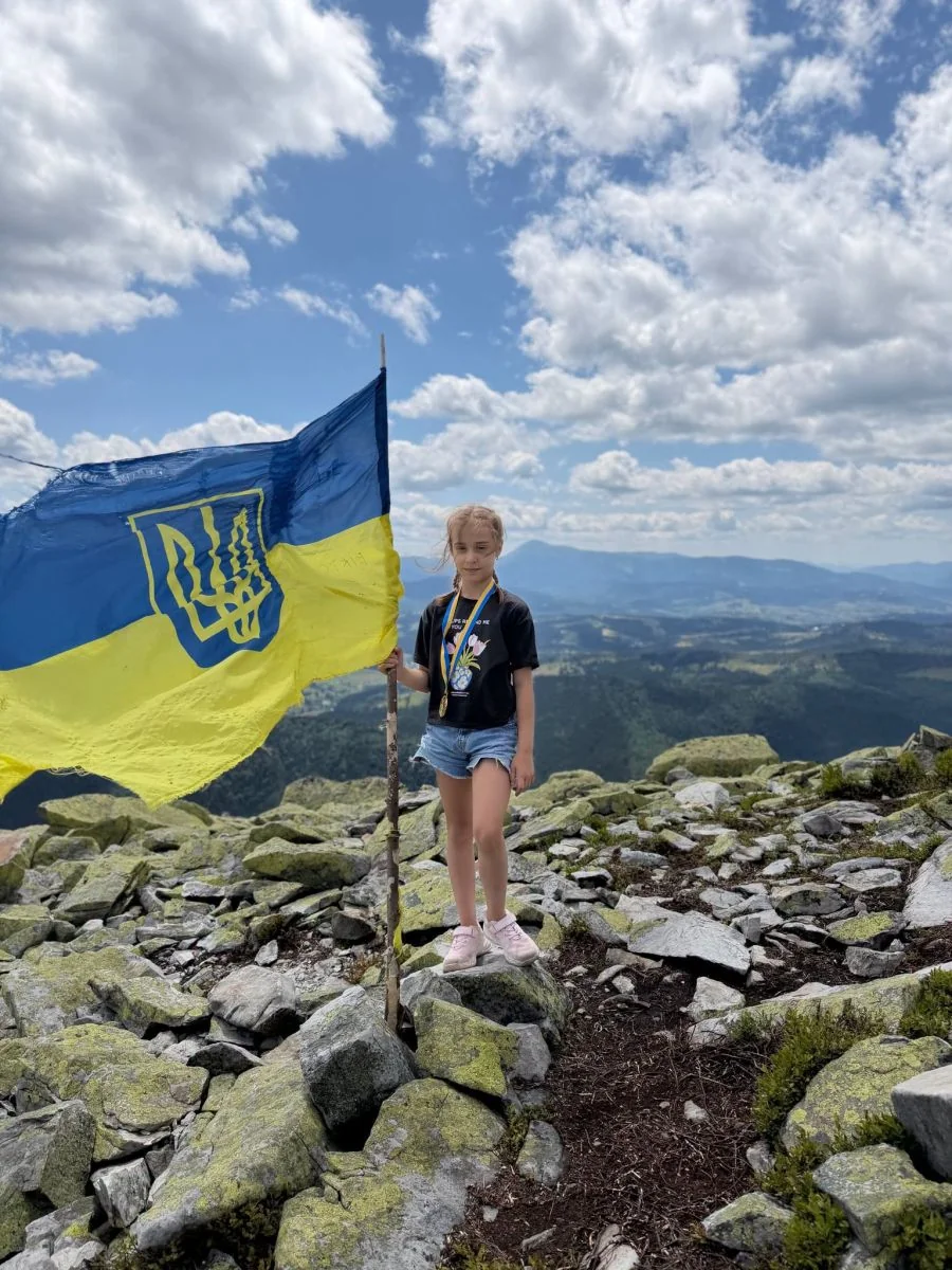 Дівчинка на кам’яній вершині Карпат тримає прапор України з тризубом