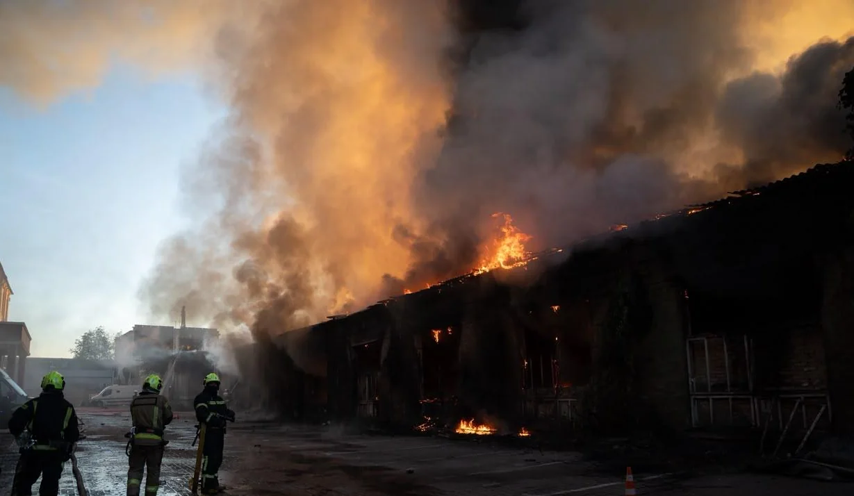 Пожежники біля палаючої промислової будівлі з густим димом і полум’ям