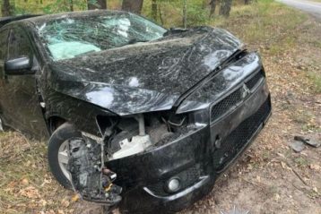 Розбитий чорний Mitsubishi Lancer на узбіччі лісової дороги біля конусів