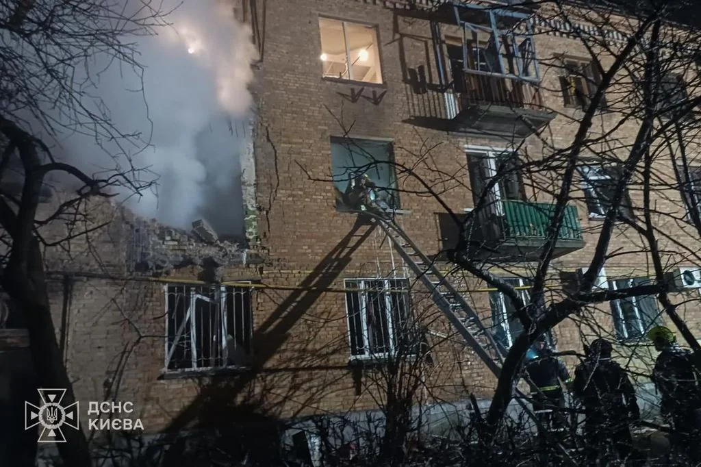 Рятувальники на драбині біля пошкодженого цегляного будинку з димом у Києві вночі