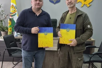 Двоє чоловіків в кабінеті тримають папки з прапором і гербом України