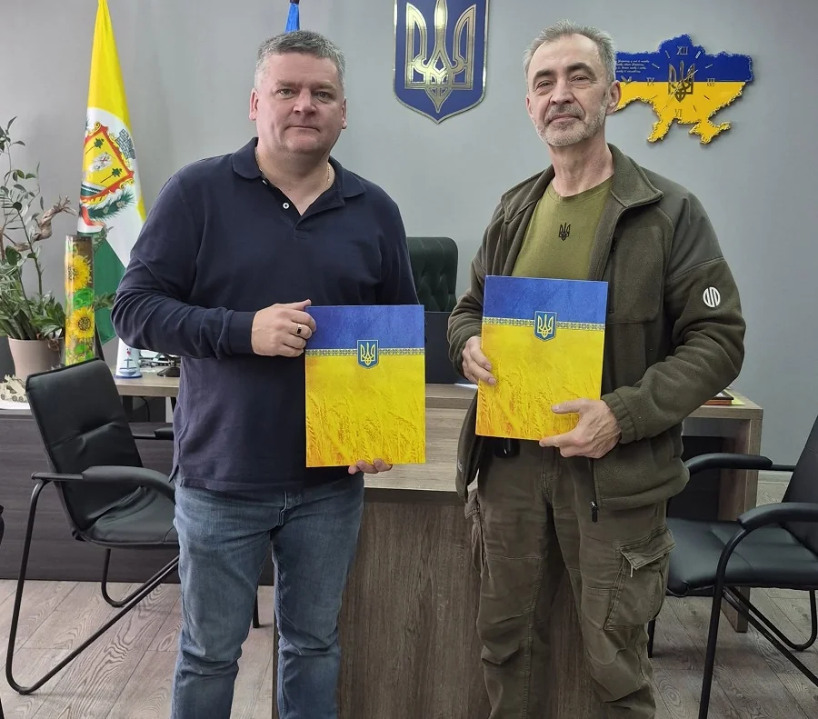 Двоє чоловіків в кабінеті тримають папки з прапором і гербом України