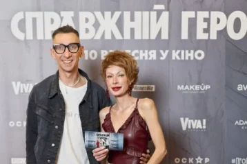 Чоловік і жінка позують біля банера фільму Справжній герой з квитком