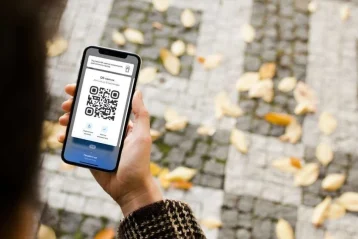 Людина тримає смартфон із QR-квитком над осіннім тротуаром