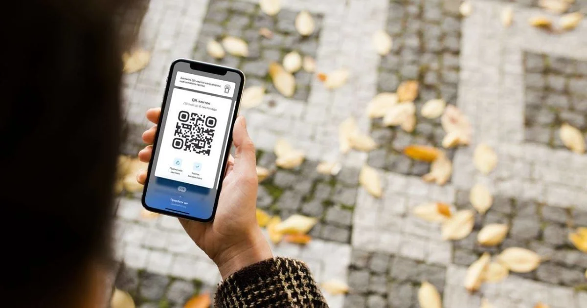 Людина тримає смартфон із QR-квитком над осіннім тротуаром