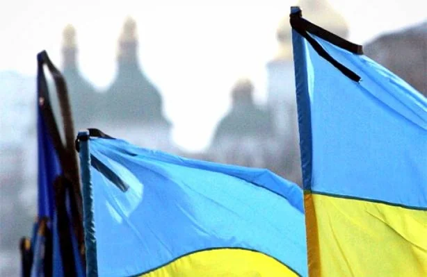 Українські прапори розвиваються на тлі розмитих золотих куполів собору