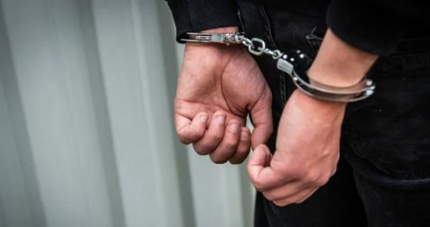 Руки чоловіка в наручниках за спиною біля сірої металевої стіни