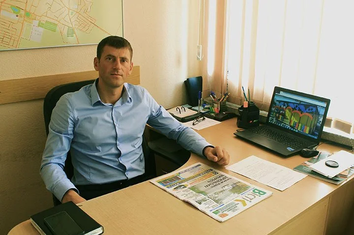 Чоловік у блакитній сорочці сидить за столом в офісі з картою міста